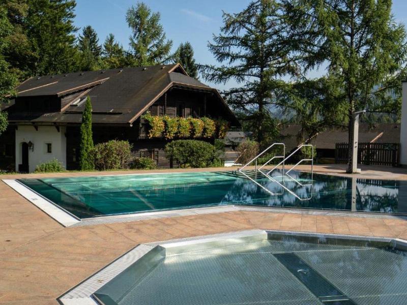Piscine extérieure et jacuzzi devant un bâtiment hôtelier entouré d'arbres.