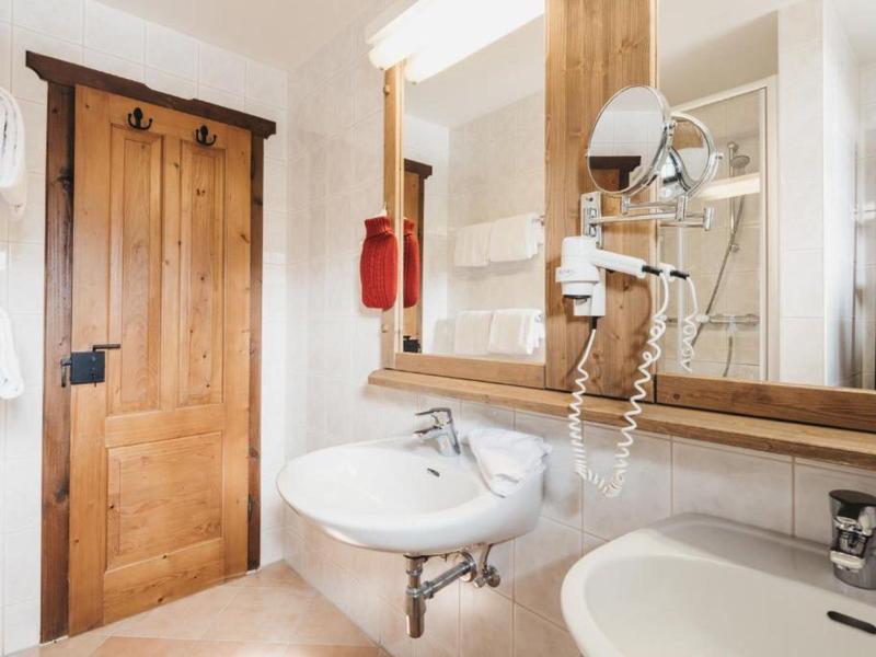 Salle de bain lumineuse avec décoration en bois, deux lavabos et un sèche-cheveux mural.