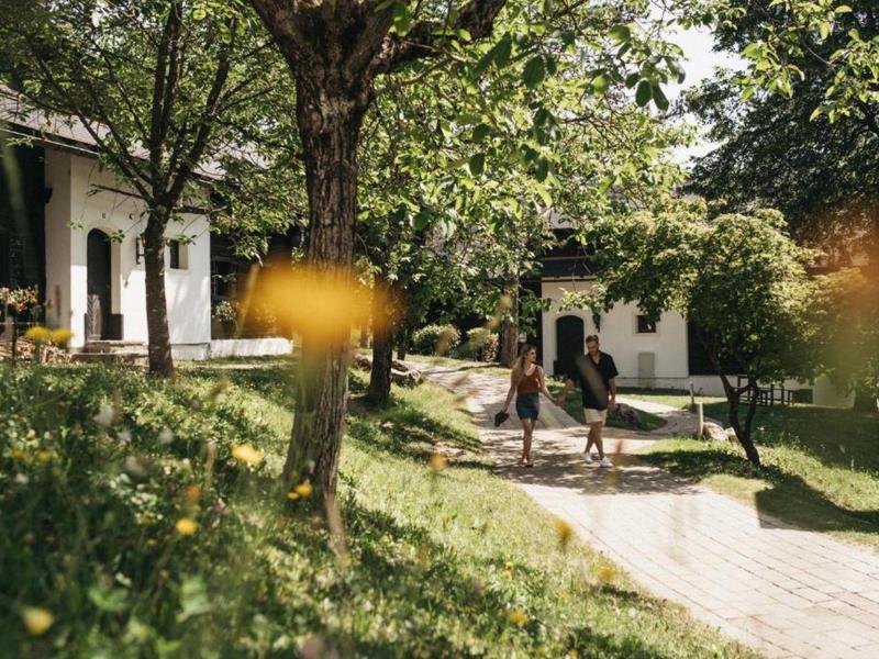 Des randonneurs se reposent sur un chemin pavé dans un jardin verdoyant avec des bâtiments blancs.