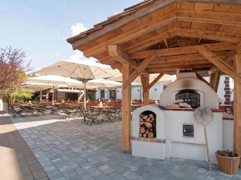 Espace extérieur couvert avec four à bois, table en bois et chaises dans un jardin d'hôtel.