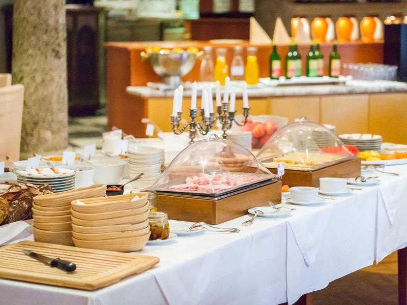 Buffet mit verschiedenen Speisen, Brotkörben und Getränken auf weiß gedecktem Tisch.