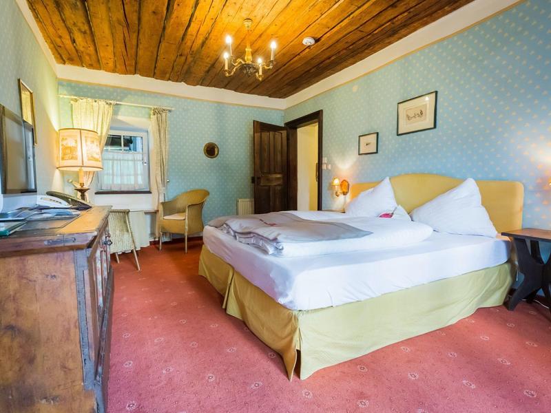 Gemütliches Schlafzimmer mit Holzbalkendecke, Doppelbett, Teppichboden und klassischem Mobiliar.