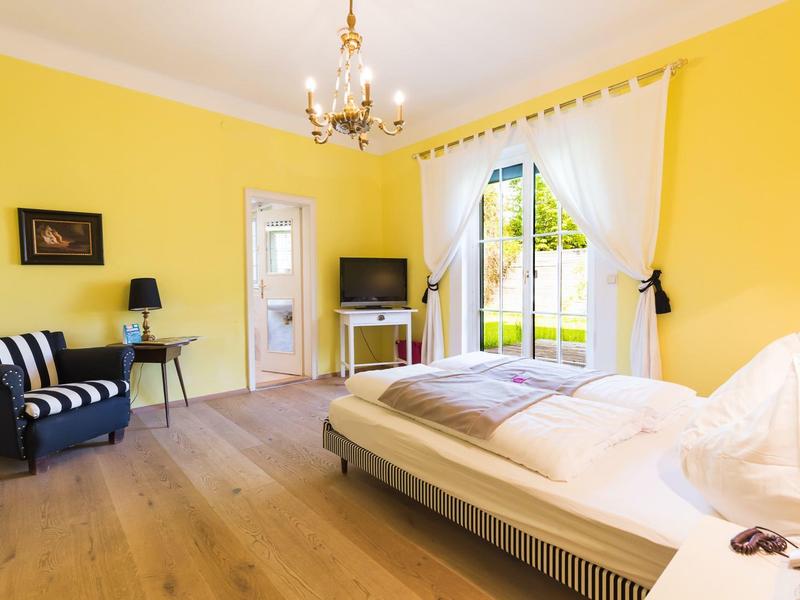 Helles Schlafzimmer mit gelben Wänden, Holzfußboden, großem Bett, Fenster, Sessel und Schreibtisch.