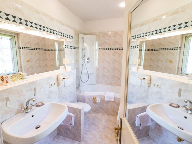 Helles Badezimmer mit zwei weißen Waschbecken, großer Spiegelwand und Duschkabine mit Fliesenrand.