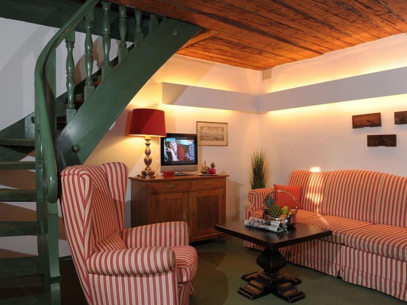 Gemütliches Wohnzimmer mit grüner Wendeltreppe, gestreiften Sesseln und Holzdecke.