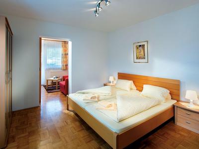 Schlichtes Schlafzimmer mit Holzbett, zwei Nachttischen und Blick ins Wohnzimmer.