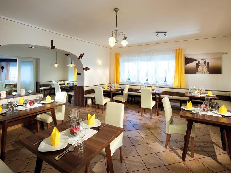 Licht restaurant met houten tafels, witte stoelen en gele accenten, klaar voor gasten.