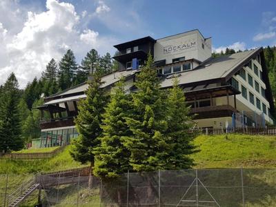 Duży budynek hotelowy na wzgórzu z zielonymi drzewami i niebieskim niebem.