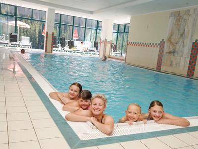 Pięcioro uśmiechniętych dzieci relaksujących się na krawędzi krytego basenu.