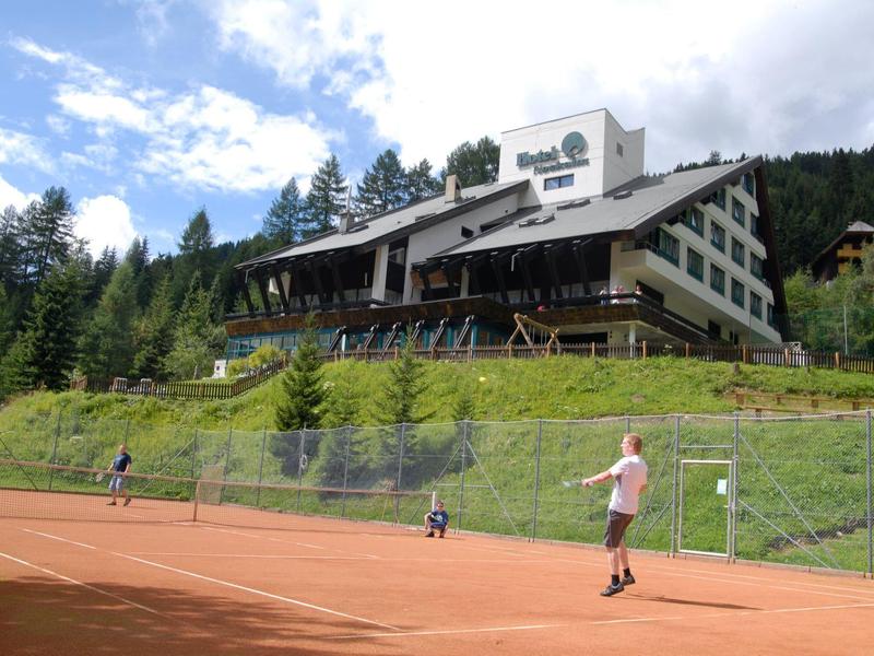 Hotel z kortem tenisowym i graczami na tle zalesionego wzgórza i niebieskiego nieba