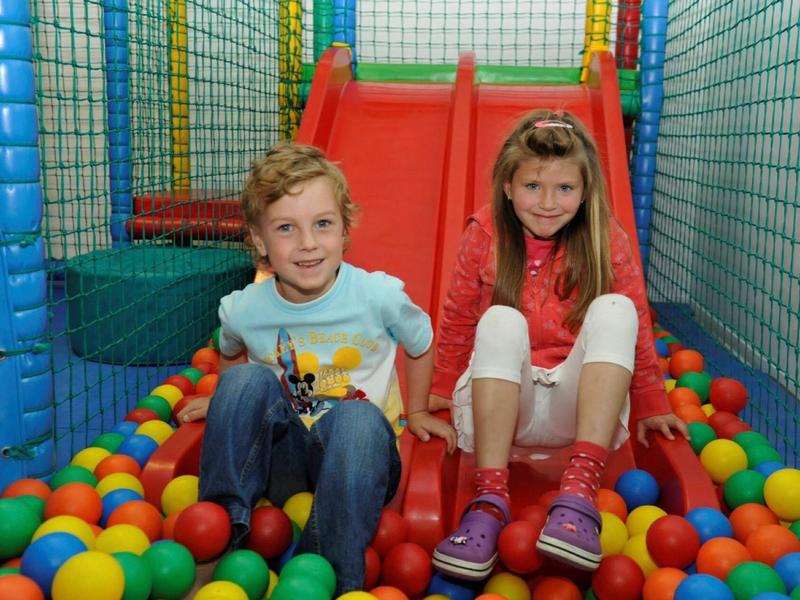 Dwoje dzieci siedzi na czerwonej zjeżdżalni w basenie z piłeczkami na placu zabaw.