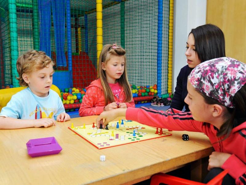 Dzieci grają w grę planszową przy drewnianym stole w kolorowej sali zabaw.
