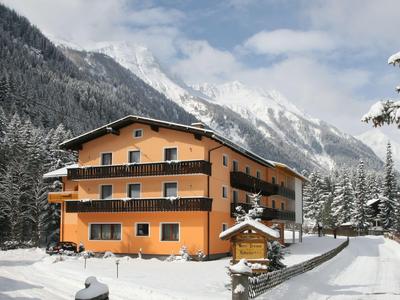 Ein orangenes Hotel in schneebedeckter Berglandschaft mit Tannenbäumen und Alpen im Hintergrund.