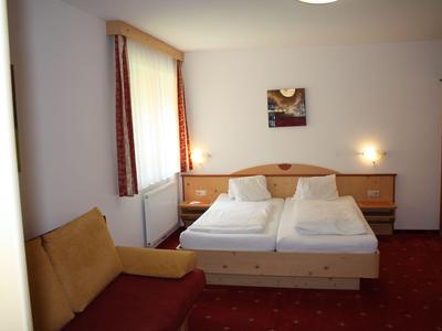 Helles Hotelzimmer mit Doppelbett, Sesseln und roten Teppichboden.
