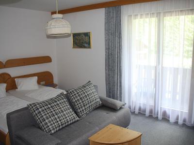 Helle Hotelzimmer mit Doppelbett, grauem Sofa, Vorhängen und Balkon mit Blick nach draußen.