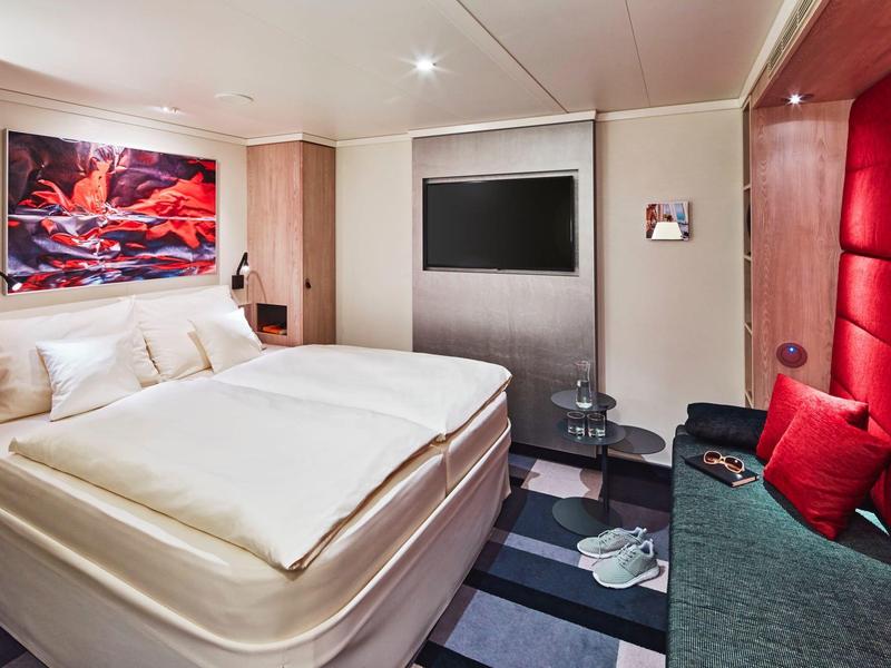 Moderne hotelkamer met groot bed, levendige rode accenten en eigentijdse kunst aan de muur.