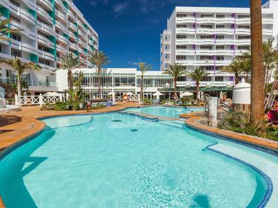 Gran piscina al aire libre entre dos edificios modernos de hotel con terraza solárium.