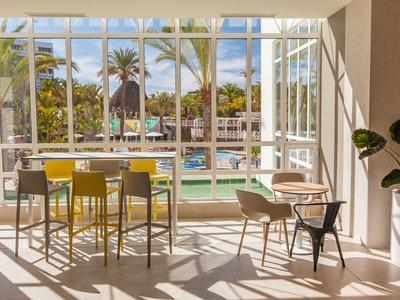 Sala iluminada con asientos y vista a la piscina y palmeras.
