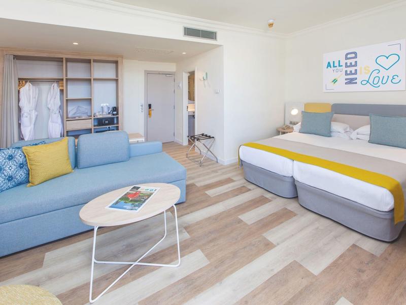 Modern hotelkamer met tweepersoonsbed, blauwe bank en lichte houten vloer.