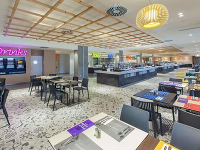 Modern gestalteter Speisesaal mit hellen Lampen, Buffet und mehreren Tischen mit bunten Platzsets.