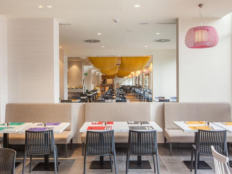 Restaurant moderne avec bancs, chaises et tables colorées sous éclairage blanc.