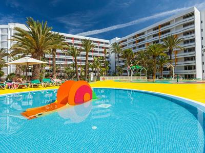 Hotel s venkovním bazénem, palmami a slunečníky pod jasnou oblohou