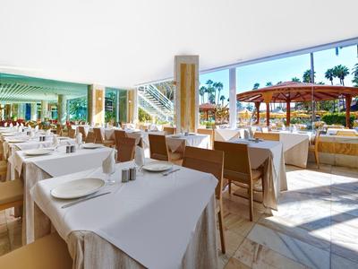 Bright outdoor restaurant with shaded tables, white tablecloths, and palm tree view.