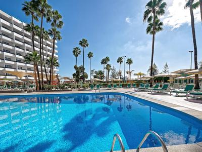 Hotel pool with lounge chairs and palm trees under clear sky