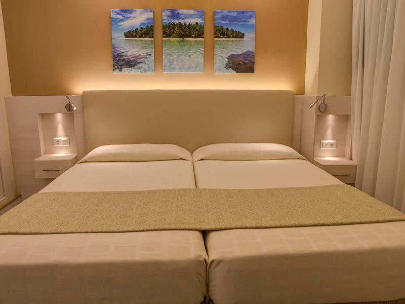 Twin beds with beige bedding in a warmly lit hotel room with art above the headboard.