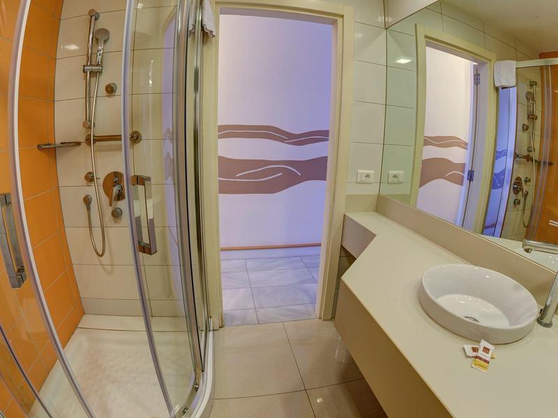 Compact bathroom with glass shower, white sink, and wooden door in a hotel room.