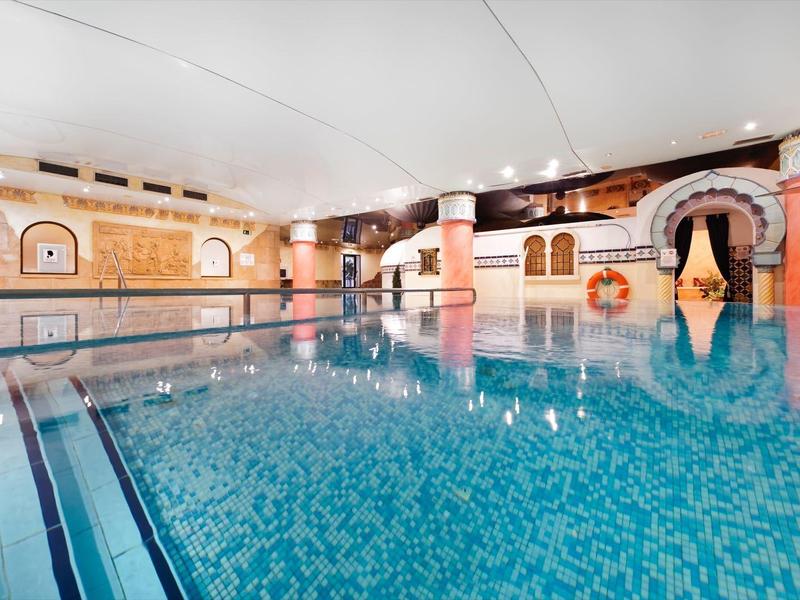 Indoor swimming pool with clear blue water, tiled walls, and lounge chairs for relaxation.