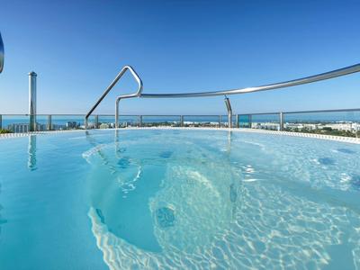 Clear blue pool water with metal handrails overlooking a distant sea and blue sky.