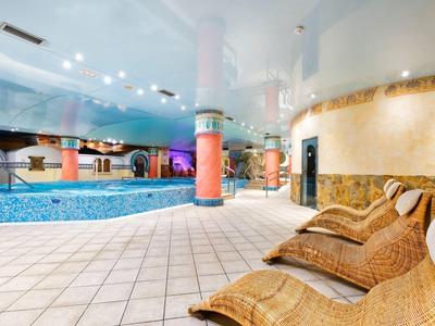 Indoor pool with lounge chairs under ceiling lights, featuring a water slide and tiled floor.