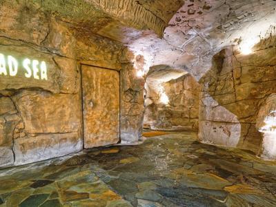 Underground cave with illuminated 'Dead Sea' sign and textured rock walls and floor.
