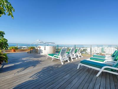 Roof terrace with sun loungers, plants, and ocean views under a clear blue sky.