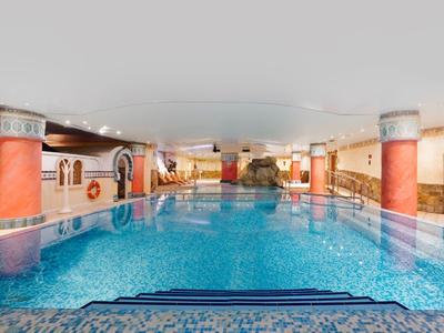 Indoor swimming pool with blue tiles, surrounded by orange columns and seating areas.