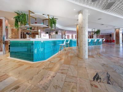 Spacious hotel lobby with turquoise tiled counters, wooden accents, and marble flooring.