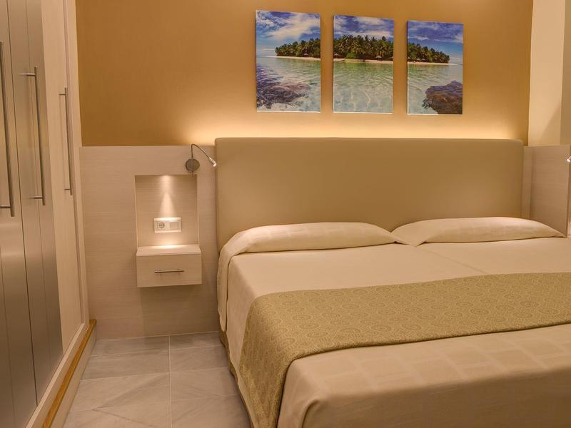 Cozy hotel room with double bed, bedside lamps, wardrobe, and triptych wall art above the bed.