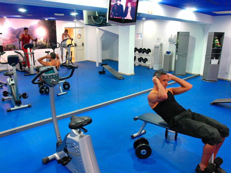 Uomo che si allena su una panca in palestra con pavimento blu e parete a specchio.