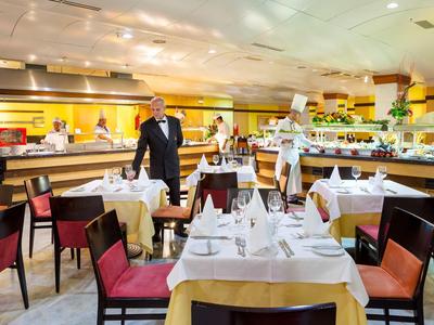 Restaurante elegante con mesas preparadas, sillas rojas y camareros con ropa negra.