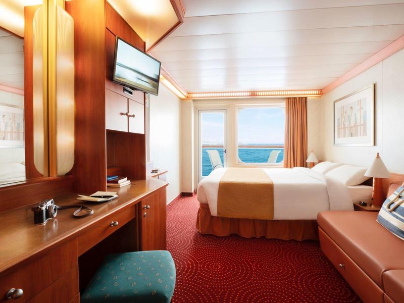 Cabina luminosa con cama doble, área de descanso y vista al mar por la ventana.