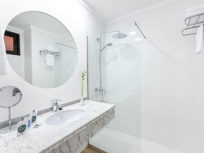 Clean modern bathroom with a round mirror, white sink, and glass shower enclosure.