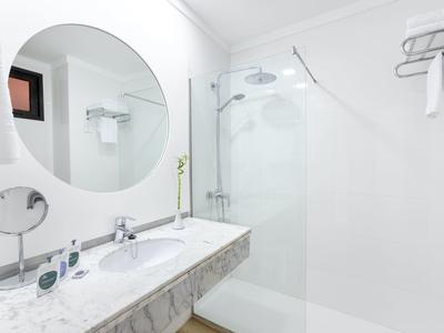 Clean modern bathroom with a round mirror, white sink, and glass shower enclosure.