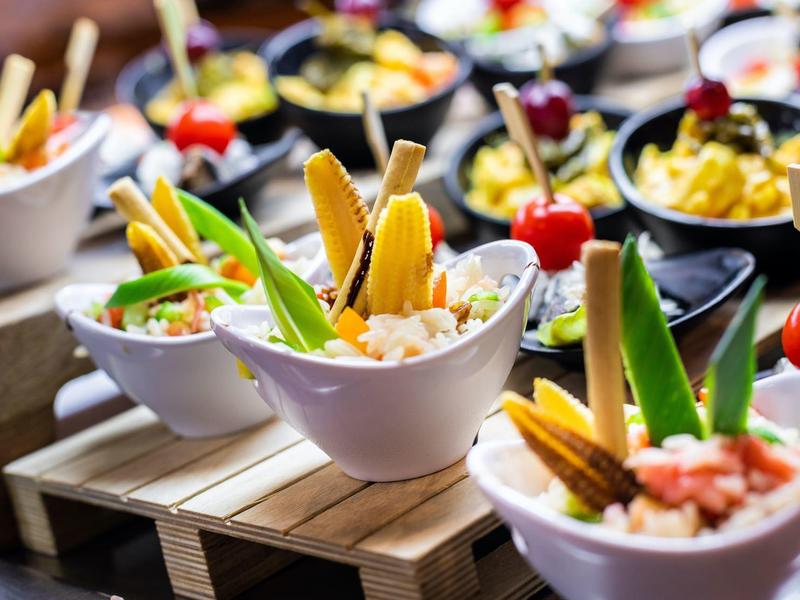 Bowls of fresh salad with vegetables and garnishes on a wooden stand.
