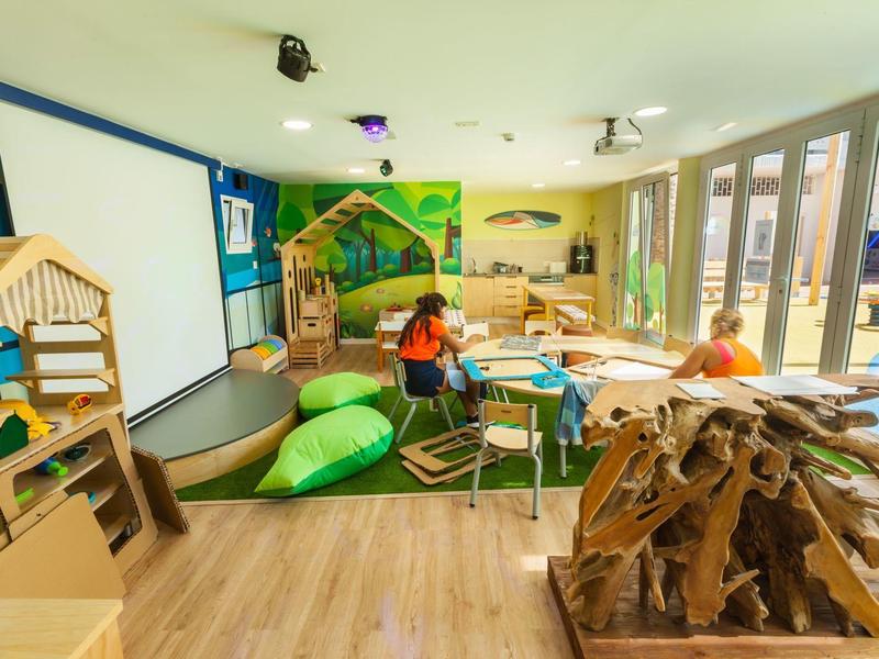 Sala giochi per bambini luminosa con mobili in legno e cuscini in un hotel.