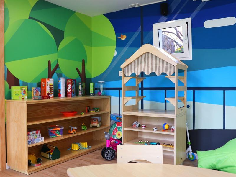 Area giochi per bambini con giocattoli in legno e scaffale contro muro colorato in hotel o casa vacanze.