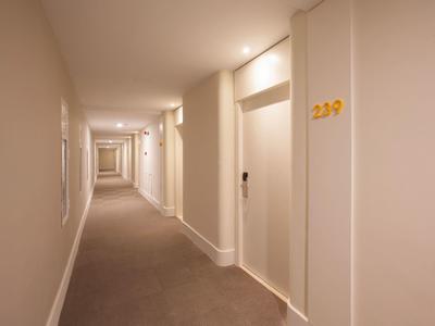 Lungo corridoio d'hotel con pareti bianche, moquette e porte con numeri di stanza