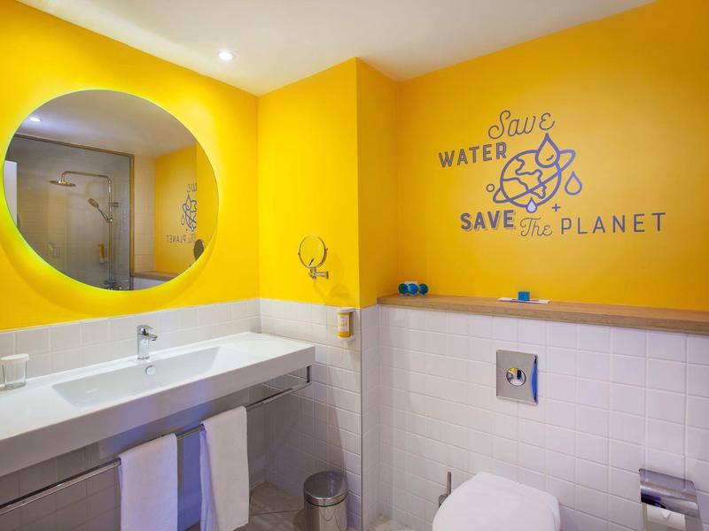 Bagno moderno con pareti gialle, grande specchio e messaggio sul risparmio idrico.