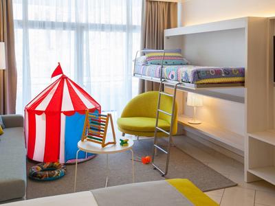 Camera per bambini con letto a castello, sedia gialla e tenda da gioco rossa vicino alla finestra.