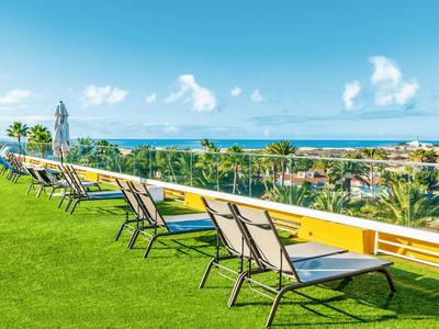 Reihen von Liegestühlen auf Rasen mit Blick auf tropische Landschaft und Meer am Horizont.